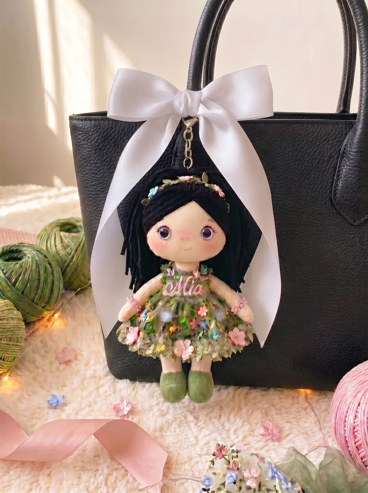 Botanical Garden bag charm with silver hardware and white satin bow on a black leather tote.