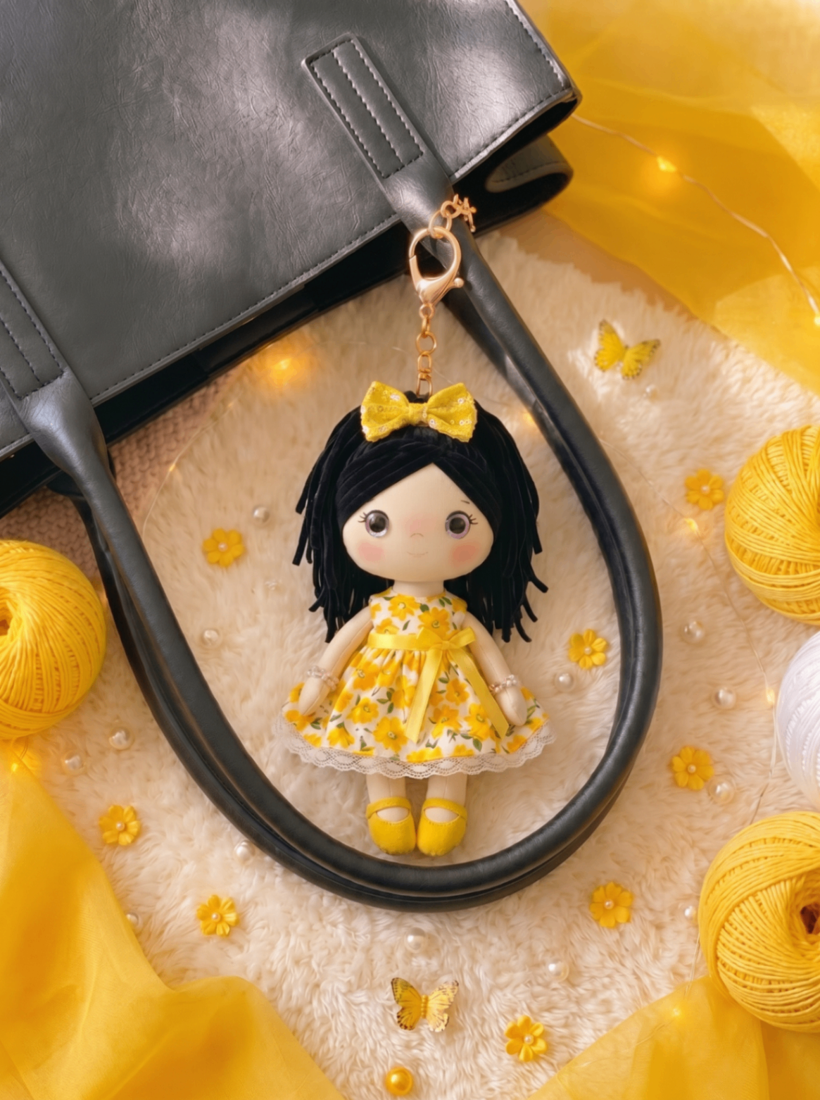 Sunshine bag charm with gold hardware shown in a flatlay next to a black tote.